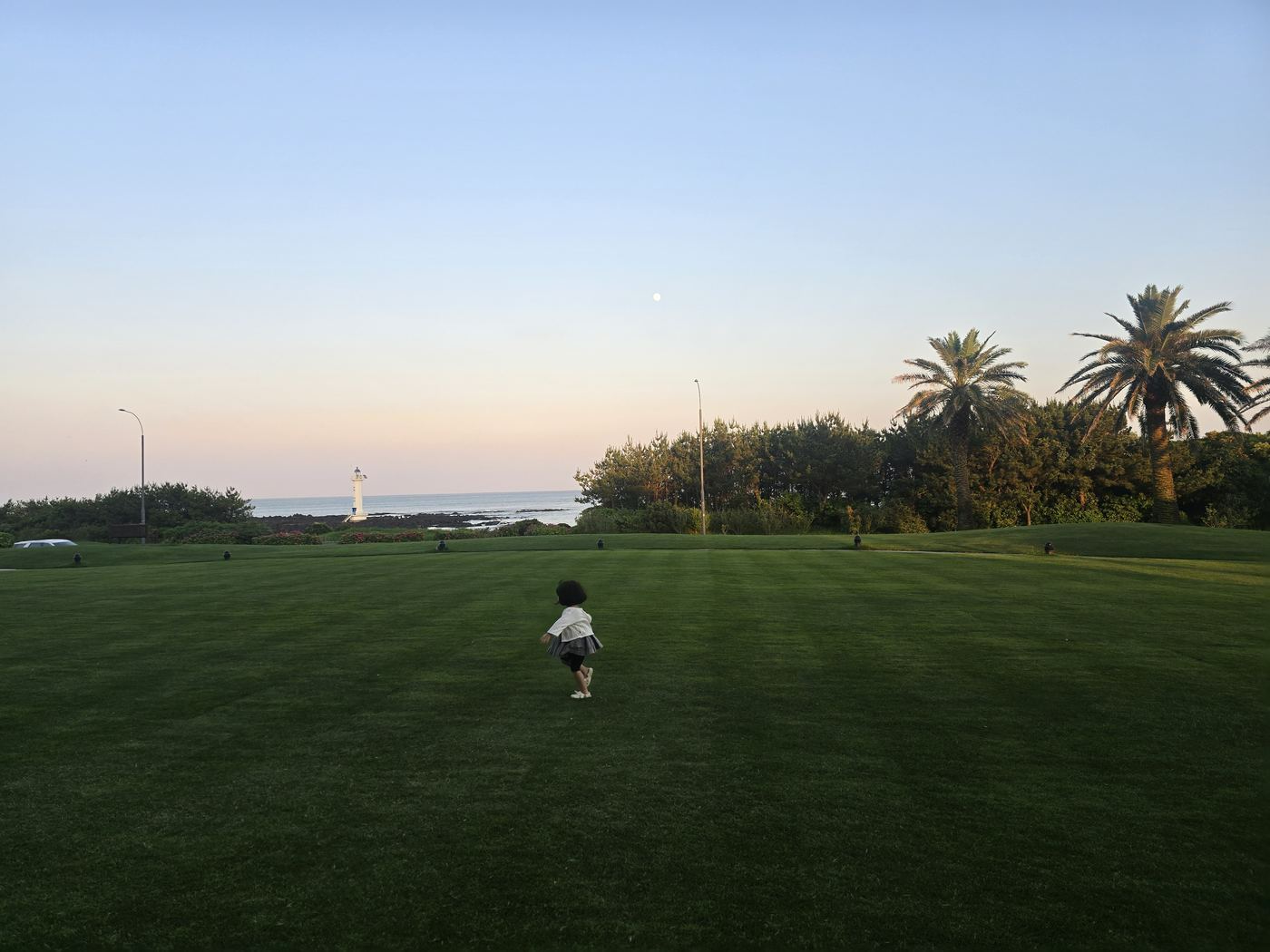 Child on resort lawn at dusk with lighthouse and sea view