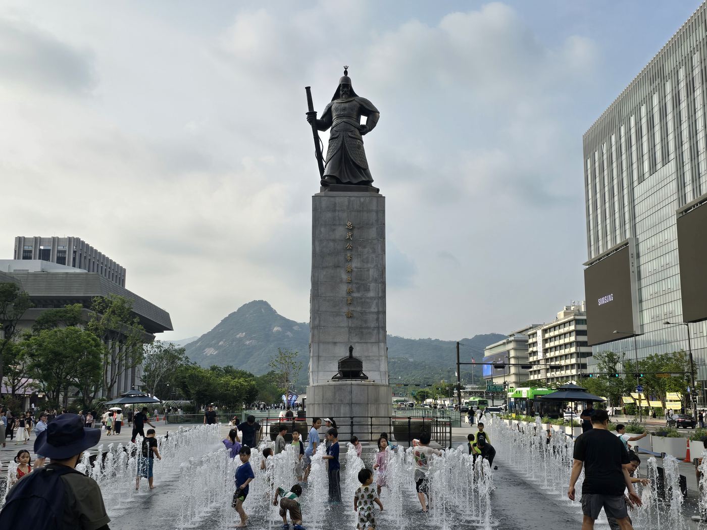 Gwanghwamun Square in Seoul at dusk — the illuminated Yi Sun-sin statue and Hangeul fountain with Gyeongbokgung visible ahead
