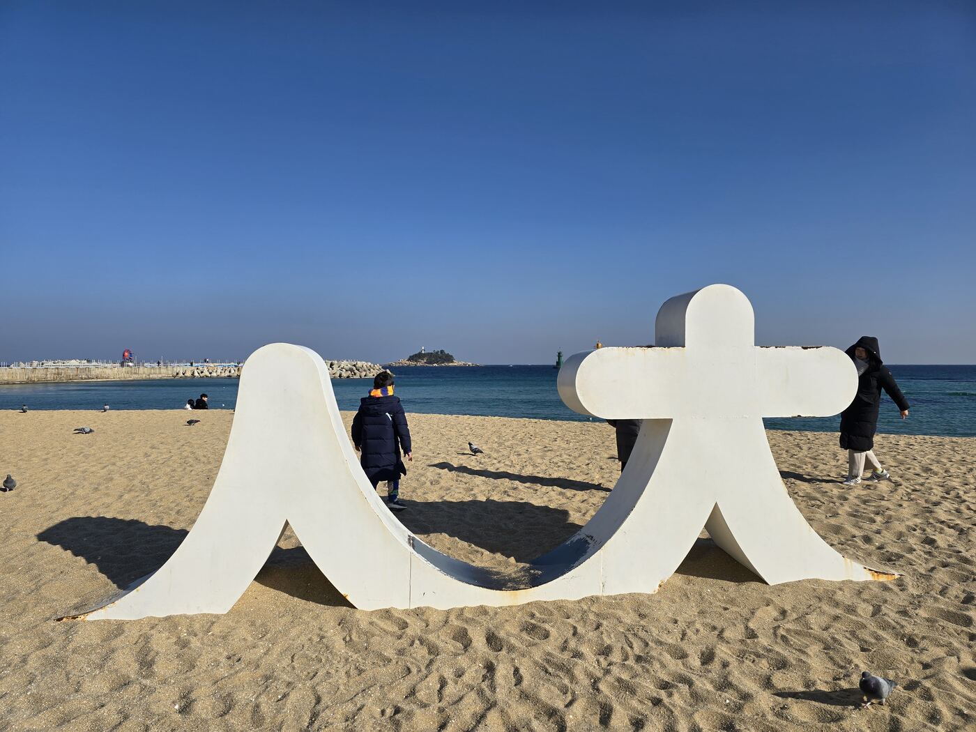 Sokcho Beach in winter with the white 人 sculpture on the sand and lighthouse in background
